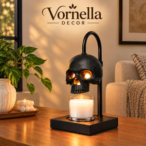 May include: A black skull-shaped candle warmer lamp with a curved arm, mounted on a square base, positioned above a clear glass jar containing a white wax candle. The text Vornella DECOR is visible at the top of the image.