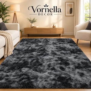 May include: A rectangular area rug featuring a shaggy, high-pile texture with a gradient color pattern transitioning between shades of dark charcoal gray, light gray, and black, covering the floor in a living room setting.