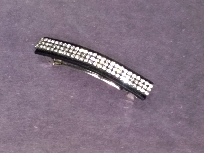May include: Black hair clip with a row of clear rhinestones.