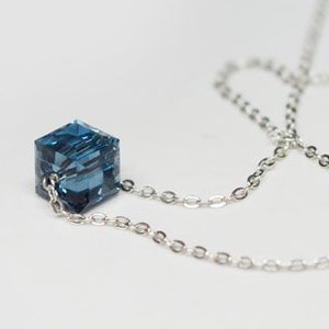 May include: A silver chain necklace with a blue crystal cube pendant. The chain has a small blue crystal bead at the clasp.