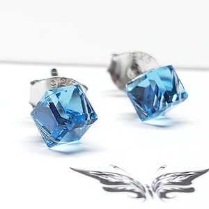 May include: A pair of silver stud earrings with light blue square-shaped crystals. The earrings are on a white surface with the text "www.michiiyuki.com Art | Jewelry | Design".
