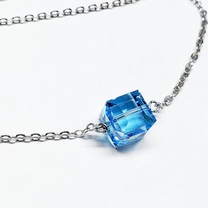 May include: A delicate silver chain necklace with a dangling blue crystal charm and a larger blue crystal cube pendant.