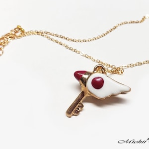 May include: Gold chain necklace with a red and white key pendant. The key has a small red circle on the top and a white wing on the side.