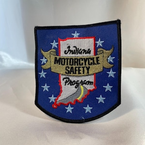 Könnte beinhalten: Blauer Aufnäher mit dem Text "Indiana MOTORCYCLE SAFETY Program" in Gold und Weiß gestickt. Der Aufnäher zeigt eine Karte von Indiana in der Mitte, umgeben von weißen Sternen.