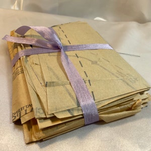 May include: A stack of brown paper sewing patterns tied together with a light purple ribbon.