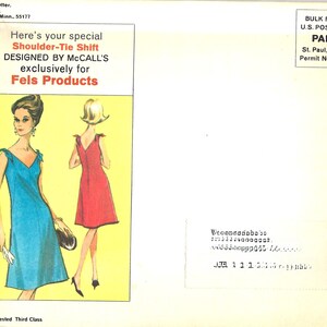 May include: A vintage sewing pattern envelope featuring a blue and red dress with a shoulder tie design. The envelope has the text "Here's your special Shoulder-Tie Shift DESIGNED BY MCCALL'S exclusively for Fels Products".
