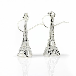 May include: A pair of silver-colored Eiffel Tower earrings. The earrings are detailed replicas of the iconic Parisian landmark, featuring intricate architectural details. The earrings have a post and hook closure.
