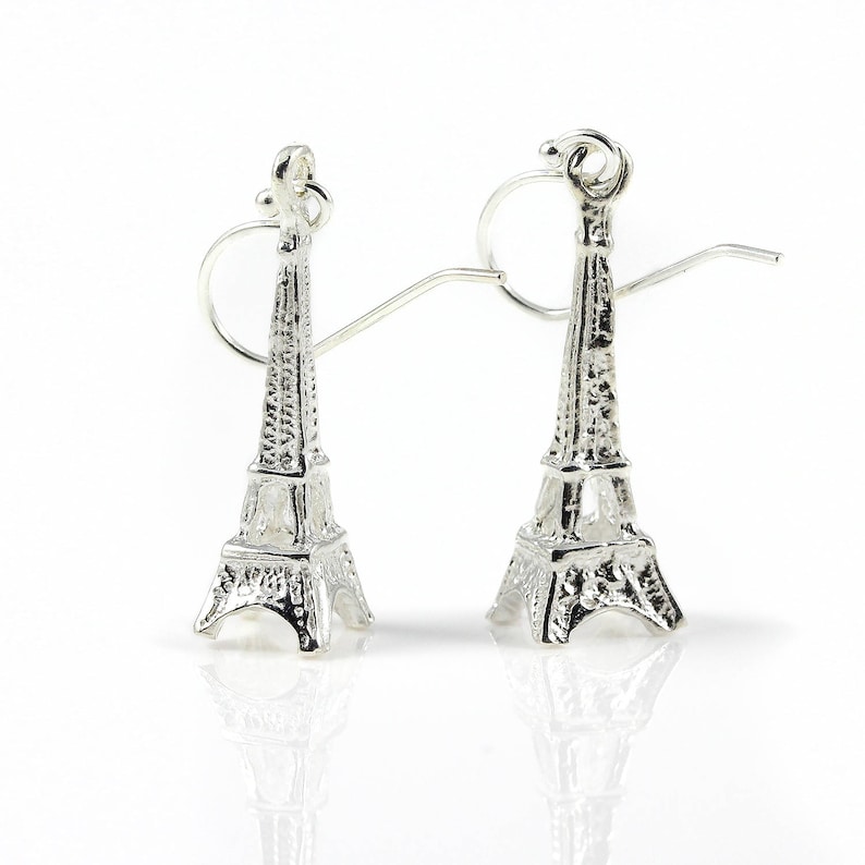 May include: A pair of silver-colored Eiffel Tower earrings. The earrings are detailed replicas of the iconic Parisian landmark, featuring intricate architectural details. The earrings have a post and hook closure.
