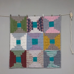 Könnte beinhalten: Eine Patchwork-Decke mit geometrischem Muster, bestehend aus Quadraten in verschiedenen Farben und Mustern, darunter Rot, Grün, Blau und Weiß.