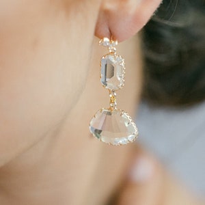 Puede incluir: Pendientes de aro dorados con tres piedras de cristal transparentes. Los pendientes tienen un diseño delicado y femenino.