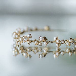 May include: A delicate gold headband with small white pearl flowers. The headband is reflected in a mirror.
