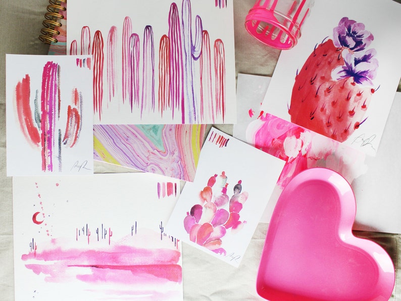 Puede incluir: Una colecci&oacute;n de pinturas de acuarela con cactus rosas y morados, un plato en forma de coraz&oacute;n rosa y una pintura de acuarela rosa y roja de un cactus con una flor.