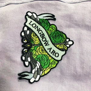 May include: Green and yellow embroidered patch with a banner that reads "Longbow Aro" on a purple denim jacket.