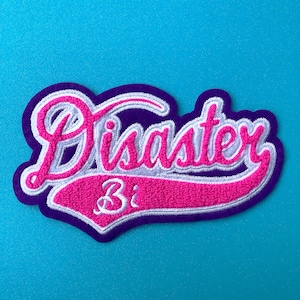 May include: A pink and white embroidered patch with the word "Disaster" in a white outline and a purple border. The word "31" is embroidered in white on a pink curved banner.