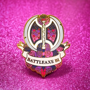May include: A gold-colored enamel pin with a white background. The pin features a double-headed axe with a pink, purple, and blue design. The axe is surrounded by pink and purple flowers. The text "BATTLEAXE BI" is written on a white banner.