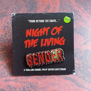 May include: A red and green enamel pin with the words "Night of the Living Gender" and the text "A thrilling enamel pin by @foxflightstudios" on a black background.