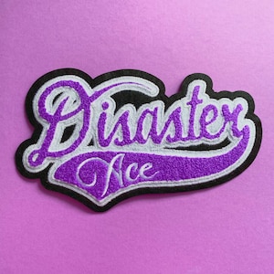 May include: Purple and white embroidered patch with the text "Disaster Ace" in a black outline.