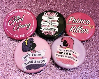 May include: Five pink, purple, and black button pins with feminist slogans. The pins feature illustrations of roses, swords, and a silhouette of a woman. The text on the pins reads: "Ohtori Academy Girl Gang Est. 1997", "Stab the Patriarchy", "Prince Killer", "Not Your Rose Bride", and "This Prince Saves Herself".