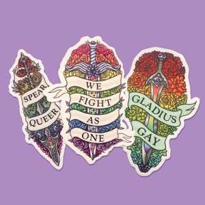 May include: Three colorful sword stickers with floral designs and rainbow colors. The stickers feature the text "Spear Queer", "We Fight As One", and "Gladius Gay".