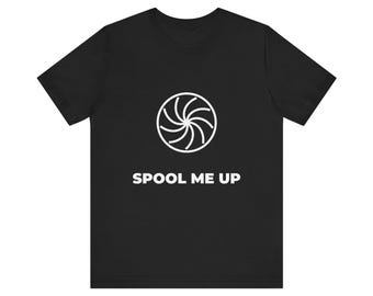 Könnte beinhalten: Ein schwarzes kurzärmeliges T-Shirt mit einer weißen kreisförmigen Grafik eines stilisierten Spulen- oder Fächerdesigns in der Mitte der Brust, wobei der Text SPOOL ME UP in weißen Großbuchstaben direkt unter der Grafik steht.