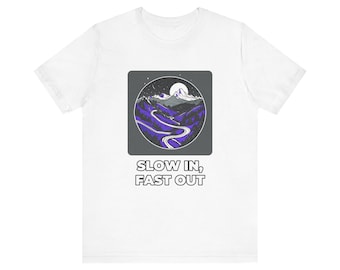 Könnte beinhalten: Ein weißes T-Shirt mit einem quadratischen Aufdruck, der eine kurvenreiche Straße durch violette Berge unter einem Mondhimmel zeigt. Unter der Grafik steht der Text SLOW IN, FAST OUT in fetten, weißen, serifenlosen Großbuchstaben.