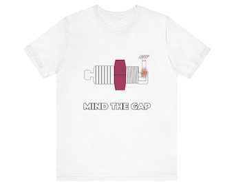 Könnte beinhalten: Ein weißes T-Shirt mit einer Grafik einer Zündkerze mit einem kastanienbraunen Mittelteil. Über dem Zündkerzenspalt ist der Text .035" mit Pfeilen dargestellt. Unter der Grafik ist der Text MIND THE GAP in fetten, schwarzen Großbuchstaben aufgedruckt.