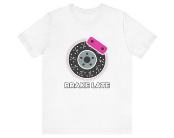 Könnte beinhalten: Ein weißes Kurzarm-T-Shirt mit einer Grafik eines schwarzen, gelochten Bremsscheibenrotors und einem pinken Bremssattel. Unter der Grafik ist der Text BRAKE LATE in einer fetten, serifenlosen Schrift auf der Brustmitte aufgedruckt.