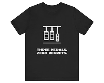 Könnte beinhalten: Ein schwarzes T-Shirt mit kurzen Ärmeln, das eine weiße Grafik von drei Autopedalen und den Text "THREE PEDALS. ZERO REGRETS." in einer fetten, serifenlosen Schrift mittig auf der Brust zeigt.