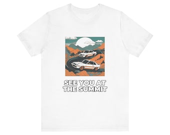 Könnte beinhalten: Ein weißes T-Shirt mit einem Grafikdruck von zwei weißen Sportwagen auf einer kurvenreichen Bergstraße. Das Motiv zeigt orangefarbene Hügel, eine große weiße Sonne und den Text SEE YOU AT THE SUMMIT in schwarzen Großbuchstaben.