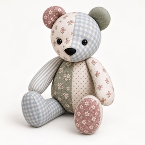 May include: A stuffed teddy bear constructed from various fabric patches featuring floral, gingham, striped, and polka dot patterns in shades of blue, green, and pink. The bear has two black button eyes and a black stitched nose, with rounded ears.