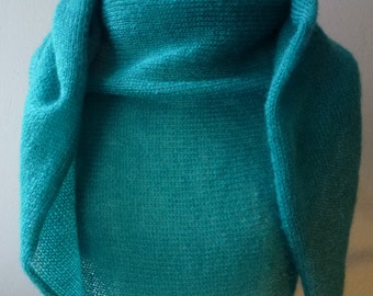 Puede incluir: Un chal tejido de color turquesa, de forma triangular. El chal se muestra, destacando su textura y diseño. La tela tejida parece suave y ligera, ideal para superponer. Mide aproximadamente 150 cm de ancho.