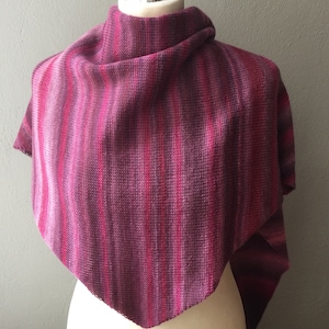 Könnte beinhalten: Ein dreieckiger gestrickter Schal in Lila- und Rosatönen mit einem gestreiften Muster.