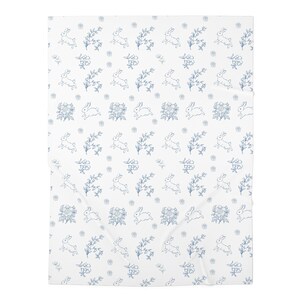Könnte beinhalten: Eine weiße Fleecedecke mit einem sich wiederholenden Muster aus blauen Strichzeichnungen. Das Design zeigt kleine Hasen in verschiedenen Laufposen, die mit detaillierten Blumenzweigen und kleinen Blüten über die gesamte Fläche verteilt sind.