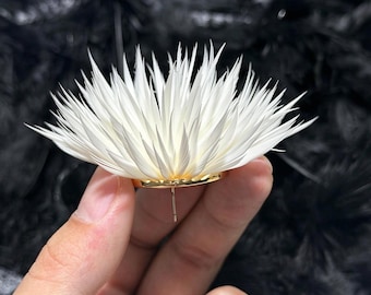 Op de afbeelding: Een witte, stekelige, bloemvormige oorbel met talloze dunne, puntige blaadjes die vanuit een centraal punt naar buiten stralen. De basis van de oorbel is een gladde, goudkleurige metalen schijf met een enkele stift in het midden.