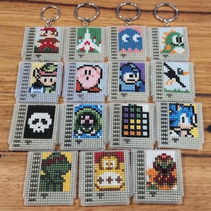 Può includere: Un set di 18 portachiavi in pixel art con vari personaggi di videogiochi classici. I portachiavi sono realizzati in plastica bianca con un anello in metallo argentato. I personaggi includono Mario, Luigi, Link, Zelda, Donkey Kong, Pac-Man, Ms. Pac-Man, Kirby, Sonic the Hedgehog, Tails, e molti altri.
