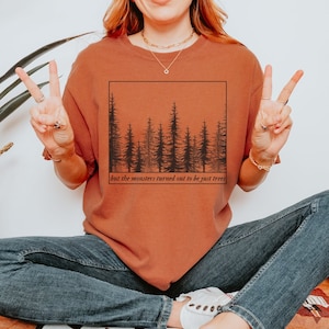 May include: A rust-coloured t-shirt with a black silhouette of a forest and the text "but the monsters turned out to be just trees".