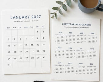 Op de afbeelding: Een witte maandplanner voor januari 2027 en een jaaroverzicht voor 2027 met donkerblauwe tekst. De maandplanner bevat een raster met de data 1 tot en met 31. Het jaaroverzicht toont alle twaalf maanden van het jaar.