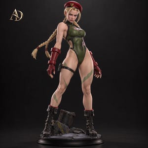 May include: A collectible figurine of a blonde character with braided hair wearing a red beret, a dark green leotard, red gauntlets, and black combat boots. The character stands on a dark, rocky base with a small metal barrel fragment.