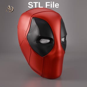 May include: A red and black mask with white mesh eye coverings, featuring the text STL File at the top. The mask has a smooth, contoured surface with visible panel lines and a distinct shape, presented as a digital 3D model design file.