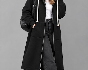 May include: A long black zip-up hoodie featuring a hood with thick white drawstrings, long sleeves with ribbed cuffs, and two front pockets. The garment is worn over a white top and dark gray wide-leg jeans with white sneakers.