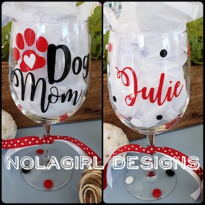 May include: Two wine glasses with black and red polka dots. One glass has a black vinyl decal that says "Dog Mom" with a red paw print and heart. The other glass has a black vinyl decal that says "Julie".