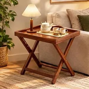 May include: A wooden folding tray table with a rectangular top and crossed legs. On the table sits a white ceramic teapot, two matching mugs, and a small plate. A table lamp with a pleated white shade stands on the left side of the tray.