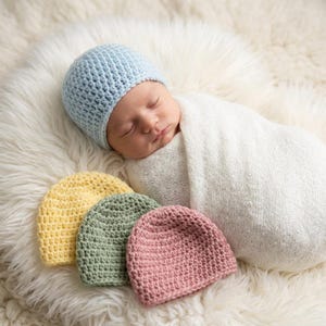May include: A newborn baby wearing a light blue crocheted beanie and wrapped in a white swaddle blanket, accompanied by three additional crocheted beanies in solid yellow, sage green, and dusty rose colours, all featuring a textured stitch.