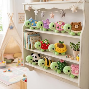 May include: A collection of crocheted turtle plushies displayed on a white wooden shelf. The turtles feature various shells including a blue star pattern, purple butterfly wings, pink flowers, a brown bear, strawberry, sunflower, panda, bee, cactus, and a pink bow.
