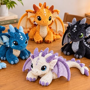 May include: Four crocheted dragon plush toys in blue, orange, black, and white with purple accents. Each dragon features large dark eyes, textured wings, and small horns. The blue dragon is on the left, orange in the back, black on the right, and white with purple on the front.