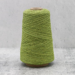 May include: A large, conical spool of vibrant lime green yarn. The thread is tightly wound around a central cardboard core, creating a textured, uniform surface. The yarn displays a consistent, bright green hue throughout the entire spool.