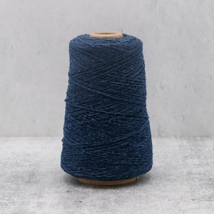 May include: A large, conical spool of dark navy blue yarn with a subtle heathered texture. The yarn is tightly wound around a central cardboard core, displaying a consistent, deep blue color throughout the entire length of the thread on the spool.