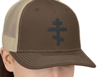 May include: A brown and beige trucker hat with a black embroidered cross on the front. The cross is a traditional Orthodox Christian symbol.