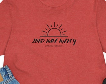 Può includere: Maglietta rossa a maniche corte con una grafica nera di un sole che sorge sopra il testo "LORD HAVE MERCY" e le parole "LAMENTATIONS 3:23".
