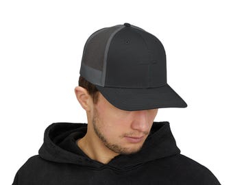 以下が含まれることがあります： メッシュバックの黒とグレーのトラッカーハット。帽子には前面に小さなロゴがあります。